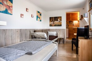 Une pièce de taille modeste comprenant un lit, un bureau, une chaise, un téléviseur et un coin cuisine.