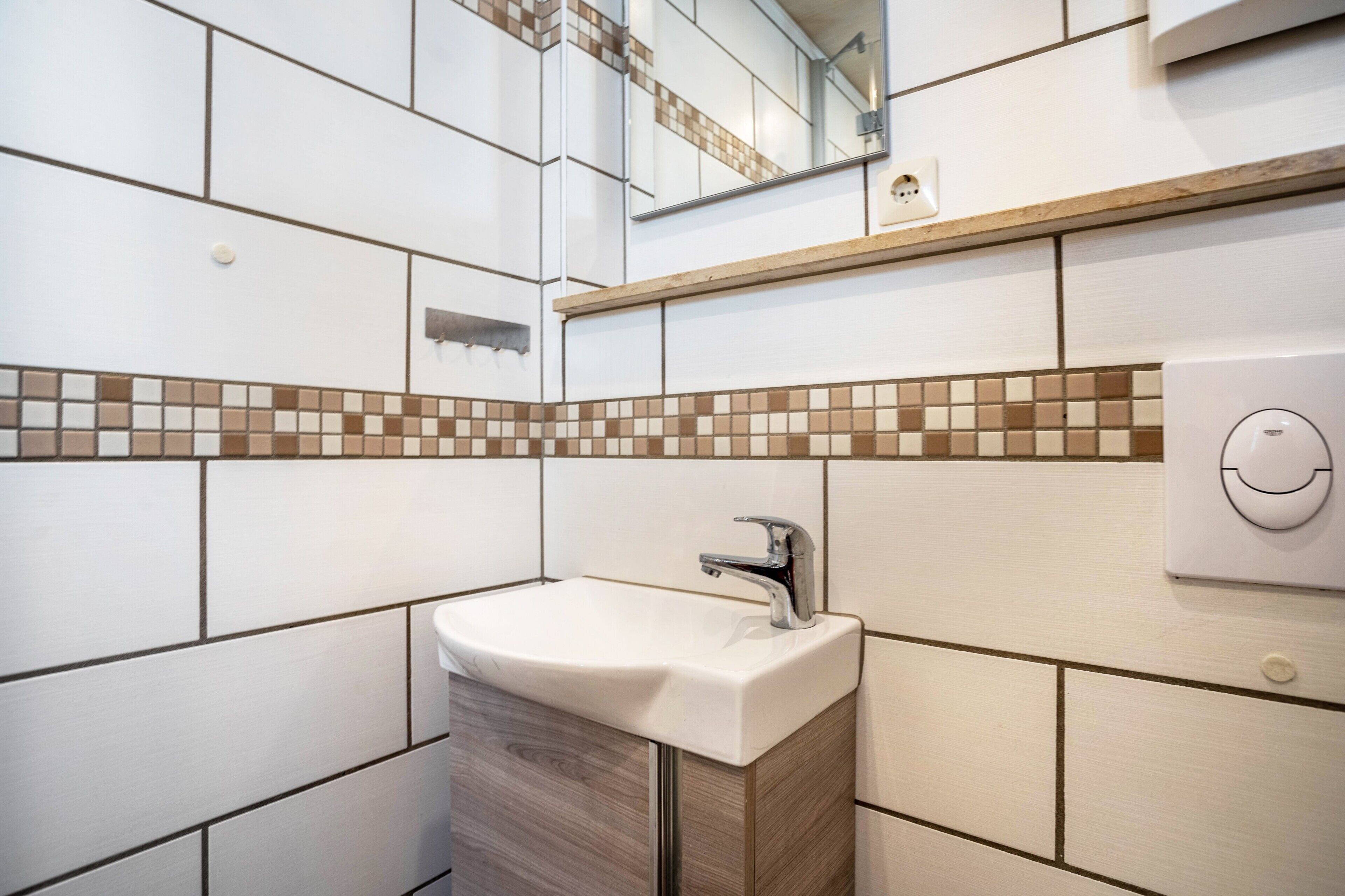 Ein Badezimmer mit einem weißen Waschbecken, einem Spiegel und einer gefliesten Rückwand.