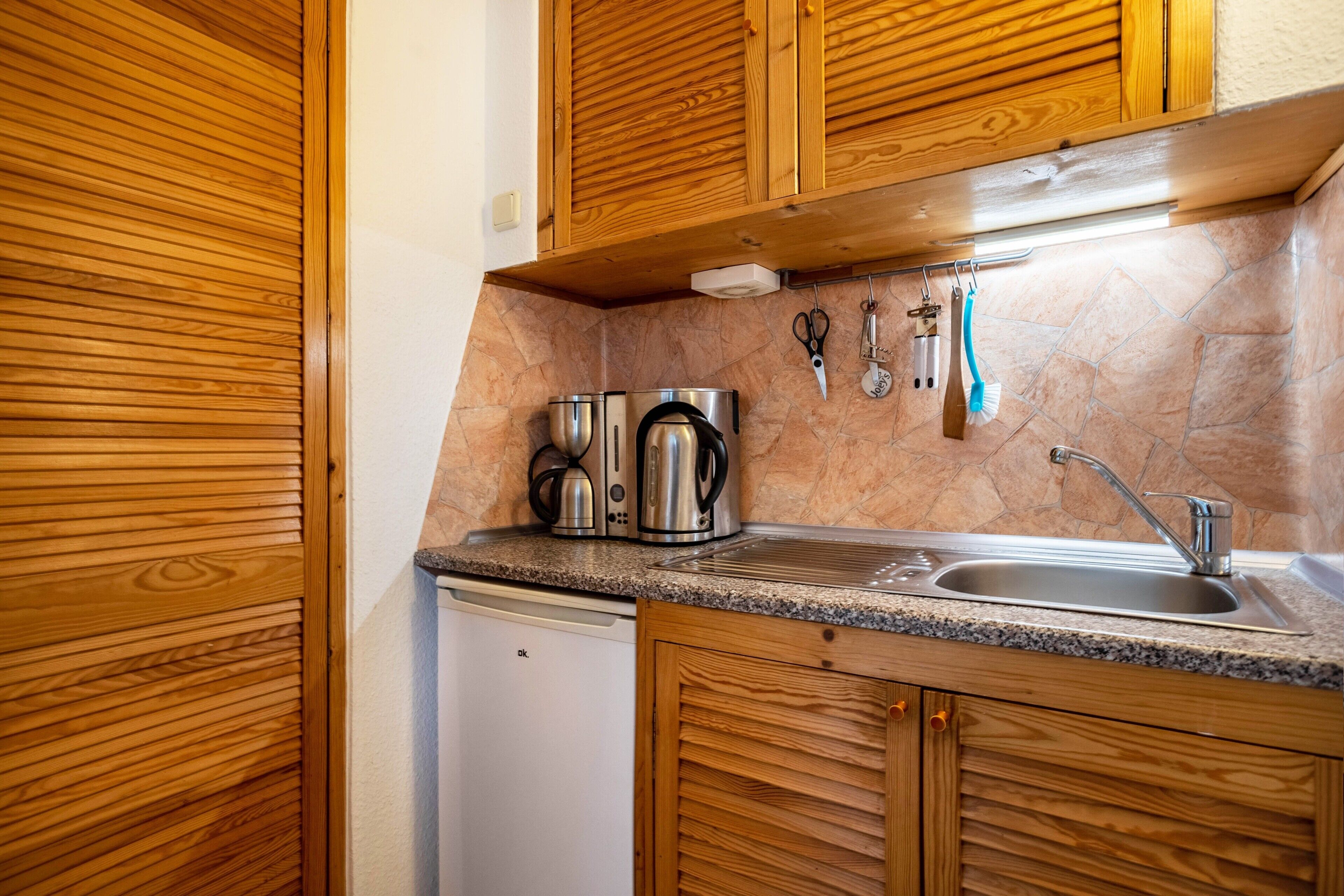 A compact kitchen with wooden cabinets, a granite countertop, a built-in dishwasher, and a stainless steel sink.