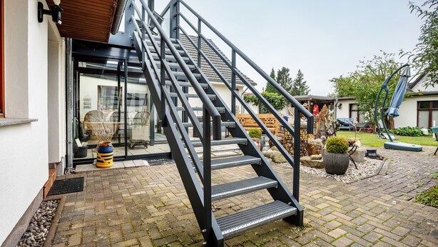 A modern outdoor staircase leading to a glass door entrance, surrounded by a paved patio with potted plants and outdoor furniture. - Apartment 'Ferienwohnung Relax' with Private Terrace, Private Garden and Wi-Fi (Stralsund)
