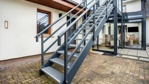 A metal staircase leading to a glass door entrance, a wooden door, and a brick-paved area. - Apartment 'Ferienwohnung Relax' with Private Terrace, Private Garden and Wi-Fi (Stralsund)