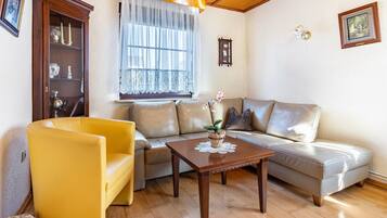 Una sala de estar con sofá, un sillón amarillo, una mesa de centro de madera y un aparador.