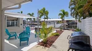 A patio with outdoor seating, a grill, and a view of a marina with boats. - Waterfront Bungalow with Pool in Matlacha Isles (Matlacha Isles-Matlacha Shores)