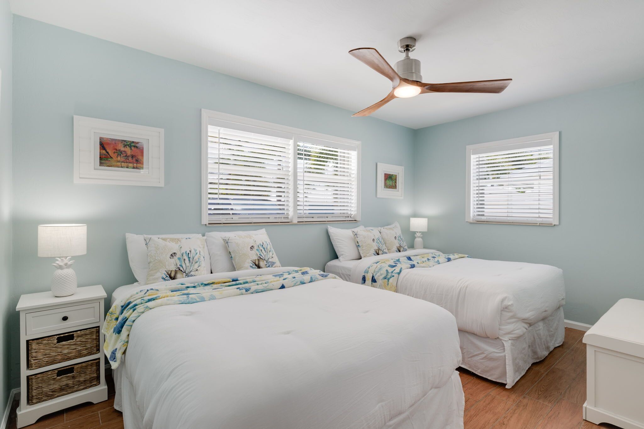 A bedroom with two beds, a ceiling fan, and two windows with blinds.