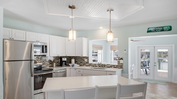 A modern kitchen with white cabinets, stainless steel appliances, and pendant lighting. - Waterfront Bungalow with Pool in Matlacha Isles (Matlacha Isles-Matlacha Shores)