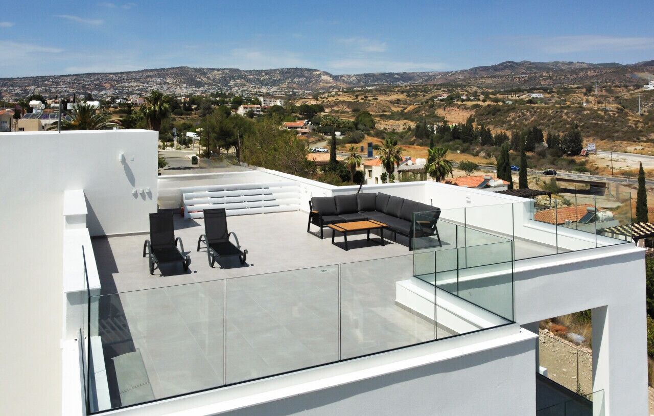 Una terraza en la azotea con barandilla de cristal, un sofá, dos sillones y una mesita.