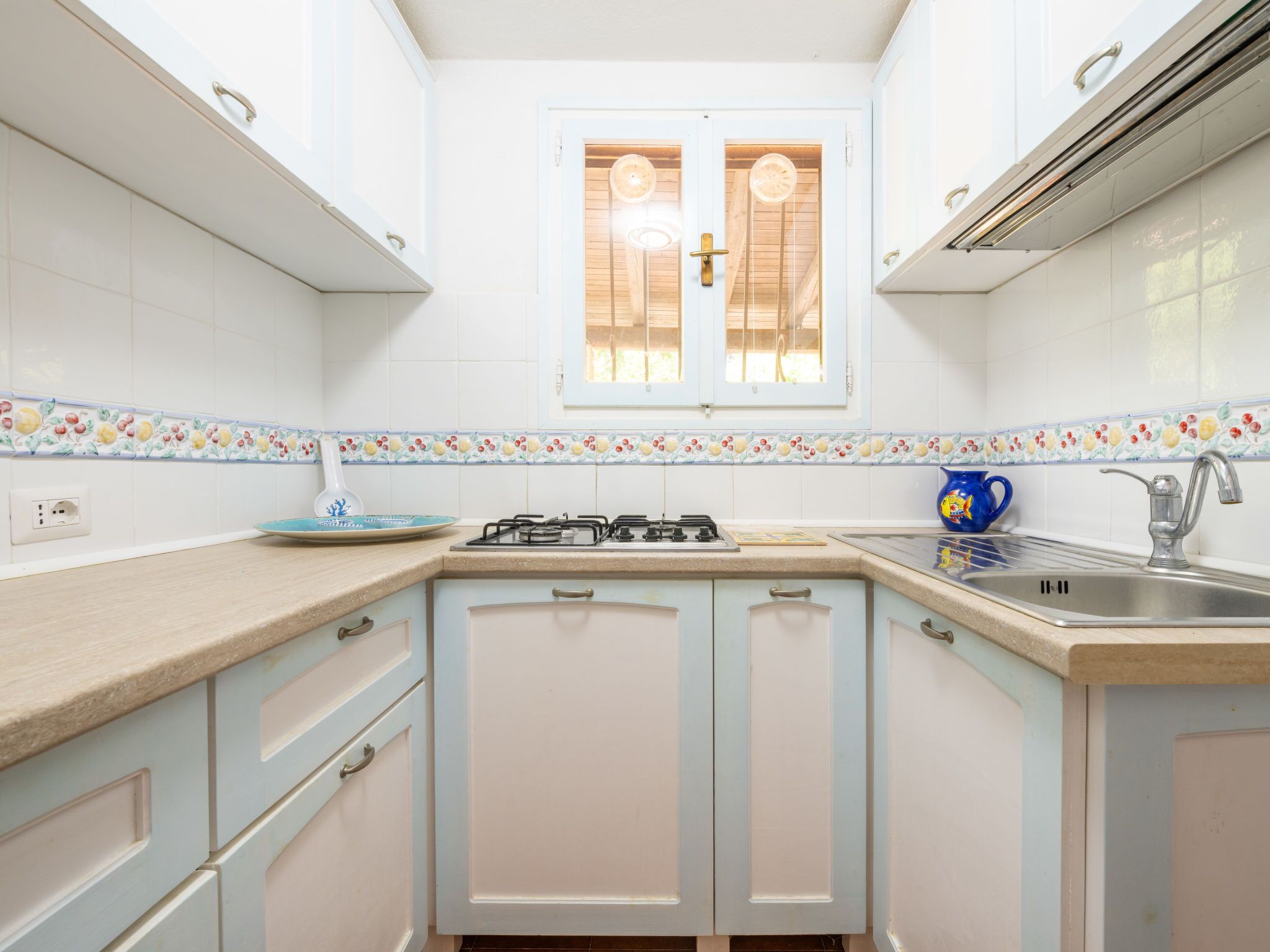 A compact kitchen with white cabinets, a gas stove, a sink, and a window with wooden shutters.