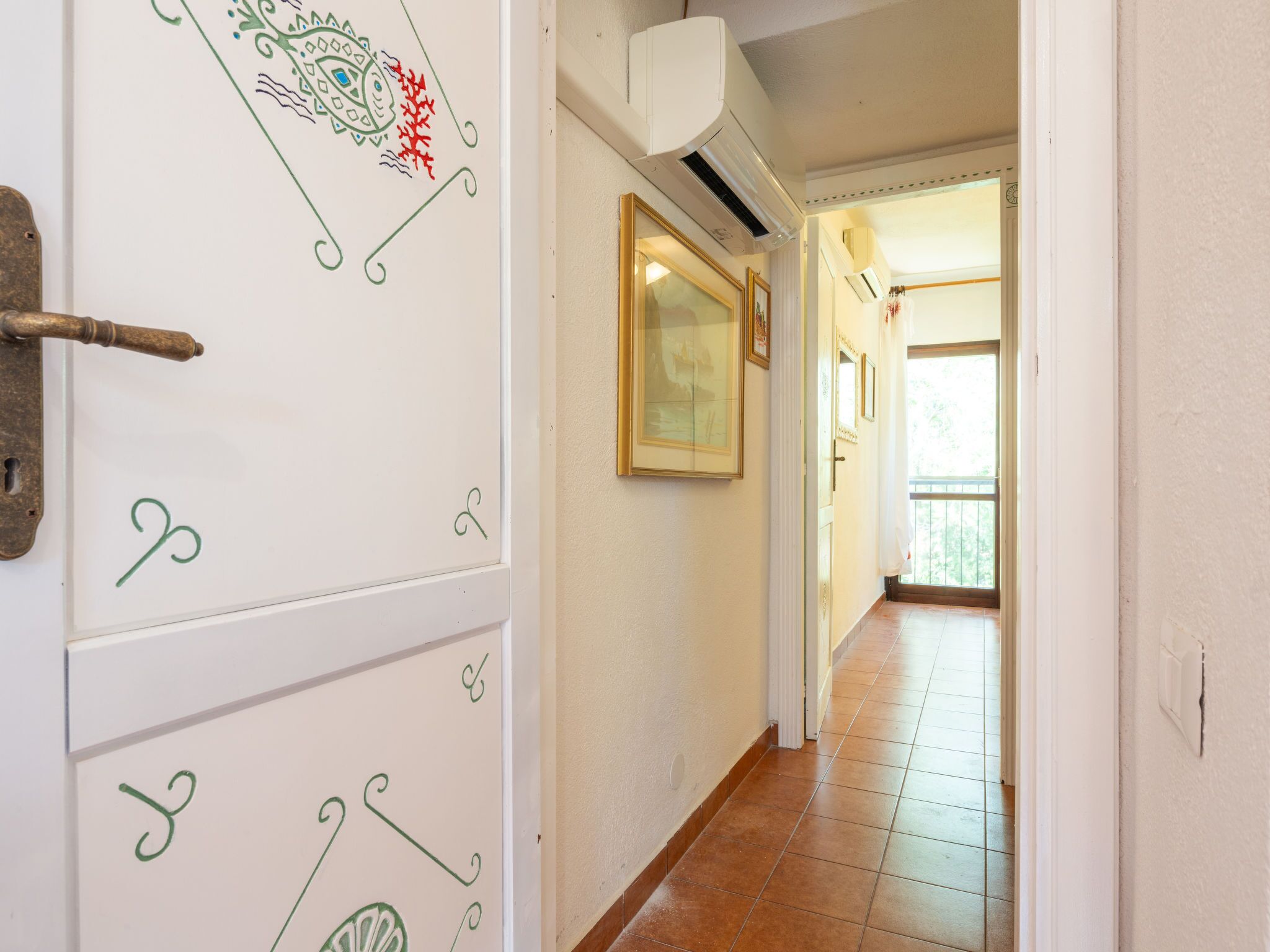 A hallway with a tiled floor, a white door with green decorative elements, and a ceiling-mounted air conditioning unit.