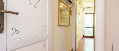 A hallway with a tiled floor, a white door with green decorative elements, and a ceiling-mounted air conditioning unit.