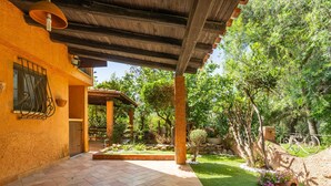 A covered patio area with a tiled floor, a pergola, and a garden with various plants and a small tree.