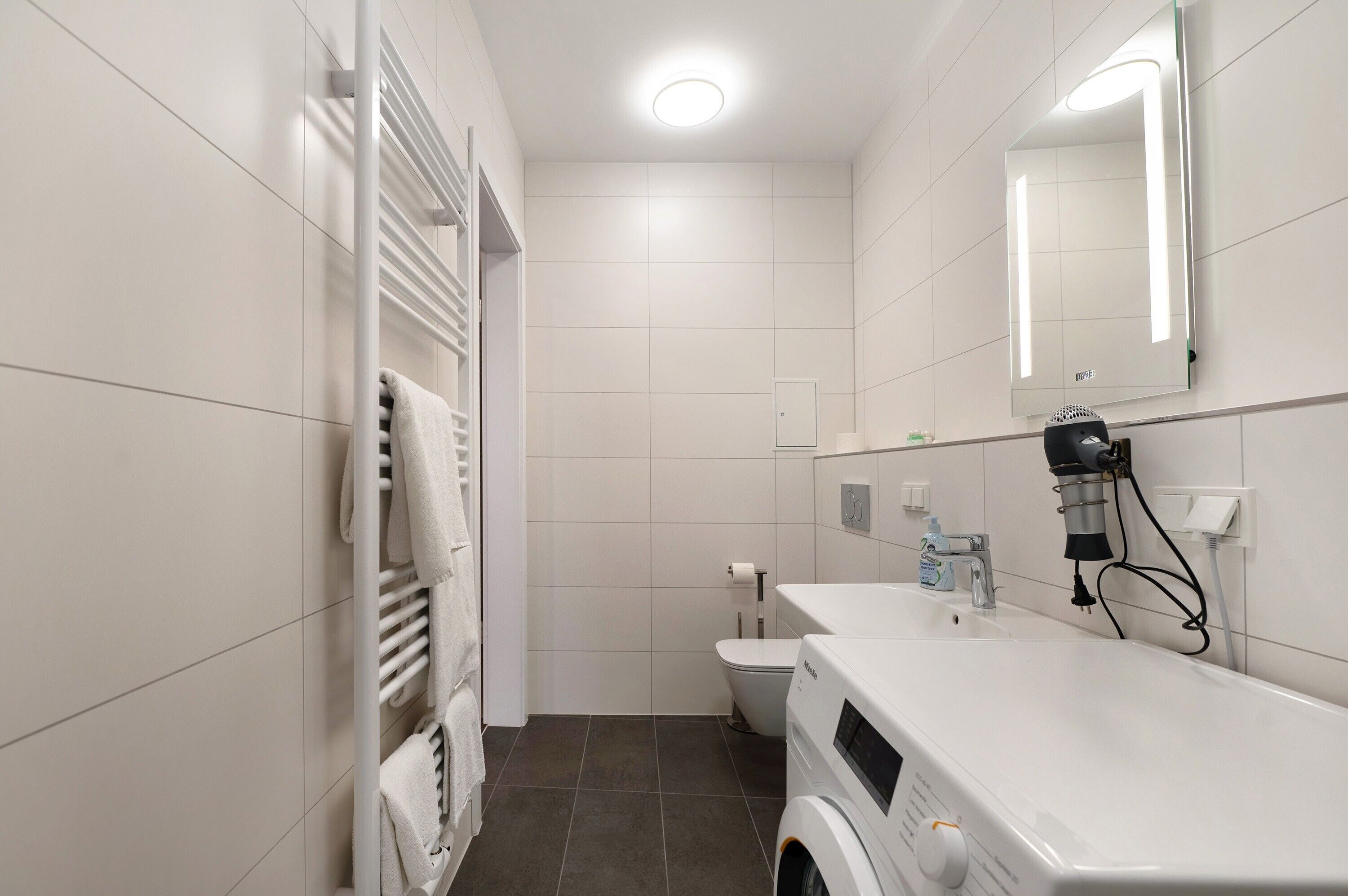 Baño compacto con lavadora integrada, toallero, inodoro y espejo.