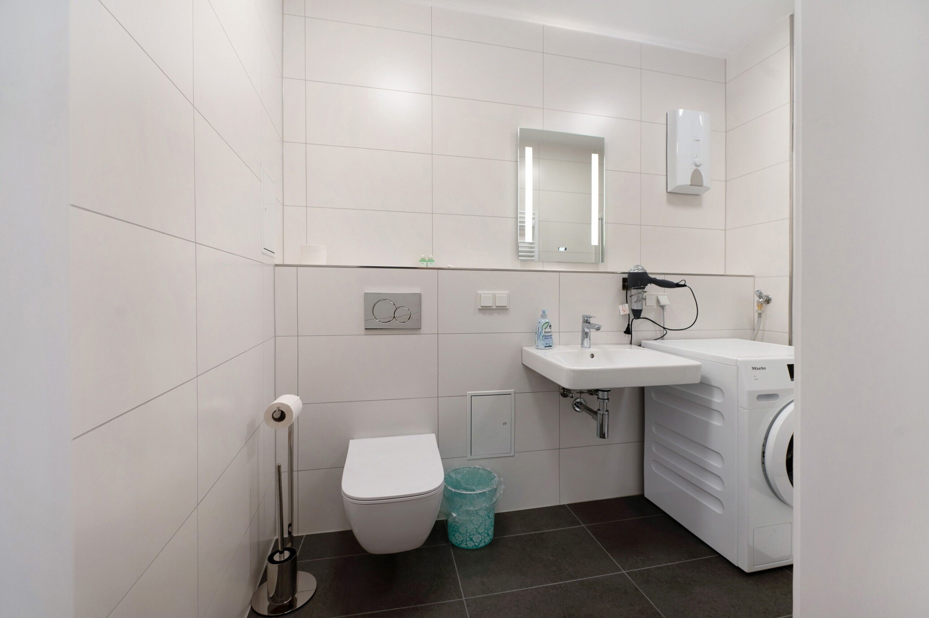 A modern bathroom with a toilet, sink, mirror, and washing machine.