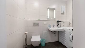 A modern bathroom with a toilet, sink, mirror, and washing machine.