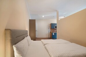Quarto de hotel com duas camas, uma cozinha compacta e uma porta que dá para outro cômodo.