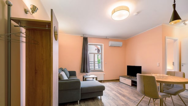 Ein modernes Wohnzimmer mit einer Couch, einem Esstisch mit Stühlen, einem Fernseher und einer Klimaanlage.