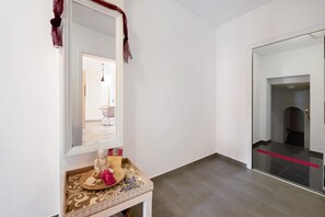 A hallway with a mirror, a small table with a Buddha statue, and a red carpet leading to a door.
