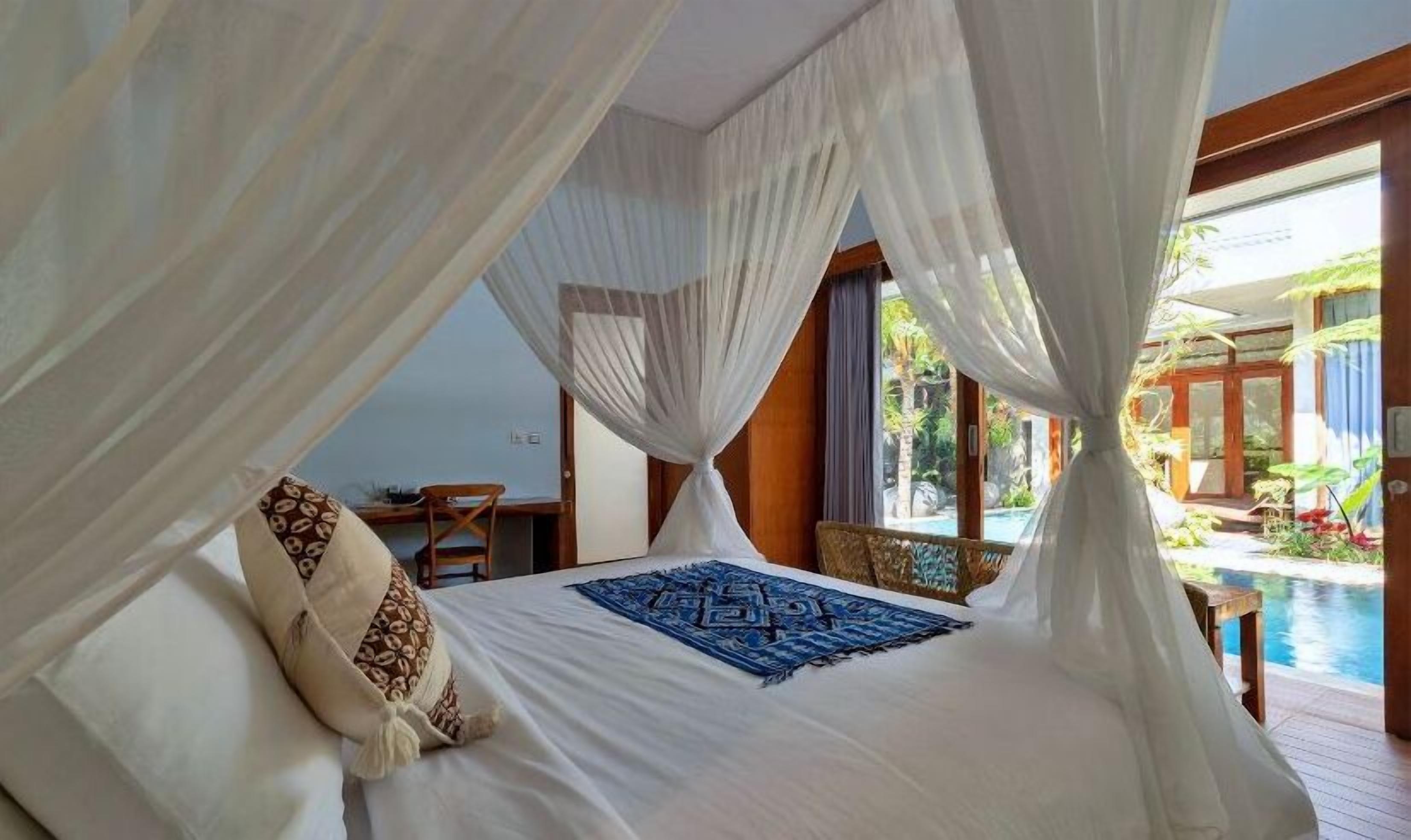 A bedroom with a canopy bed, a view of a pool, and a dining area visible through the window.