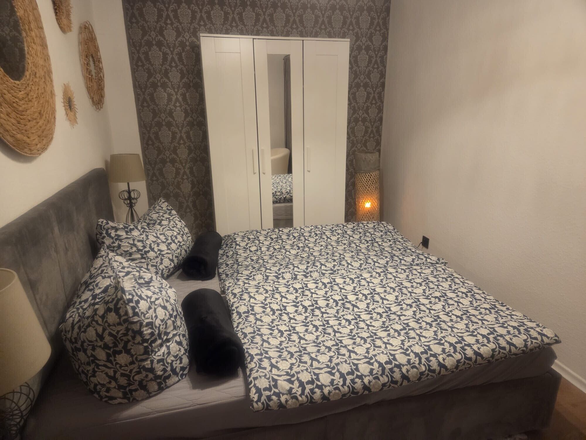 Ein Schlafzimmer mit Bett, Kissen, Kleiderschrank, Lampe und Wandbild.