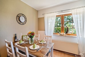 Een eetkamer met een houten tafel voor vier personen, witte stoelen, een wandklok en een raam met gordijnen.