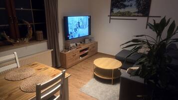 A living room with a TV, wooden furniture, a plant, and a framed picture on the wall.