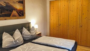 Ein Schlafzimmer mit Bett, Kissen, einem Nachttisch, einer Lampe, einem Holzschrank und einem Bild an der Wand.