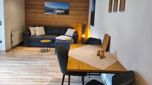 Ein gemütliches Zimmer mit Holzbalkendecke, einer Couch mit Kissen, einem kleinen Tisch und einem Bild an der Wand.