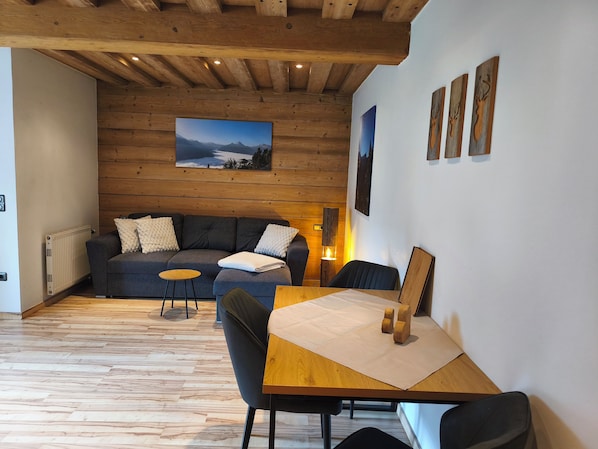A cozy room with a wooden ceiling, a sofa with cushions, a small table, and a painting on the wall.