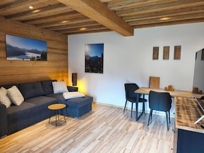A modern interior with a wooden ceiling, a sofa, a small table, a dining area, and wall-mounted artwork.