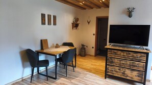 Ein Essbereich mit einem Holztisch, schwarzen Stühlen, einem Fernseher auf einem Holzständer und einem an der Wand befestigten Hirsch-Dekoration.