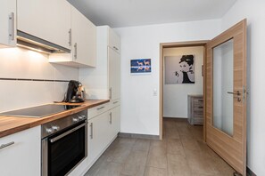 Une cuisine moderne avec des armoires blanches, un plan de travail en bois et un four. Un tableau est accroché au mur et une porte donne accès à une autre pièce.