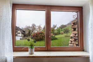 Une fenêtre donnant sur un paysage verdoyant, un mur de pierre et un bâtiment en arrière-plan.