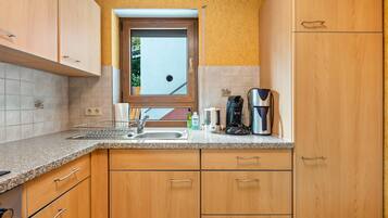 A kitchen with wooden cabinets, a window, a sink, and a coffee maker.