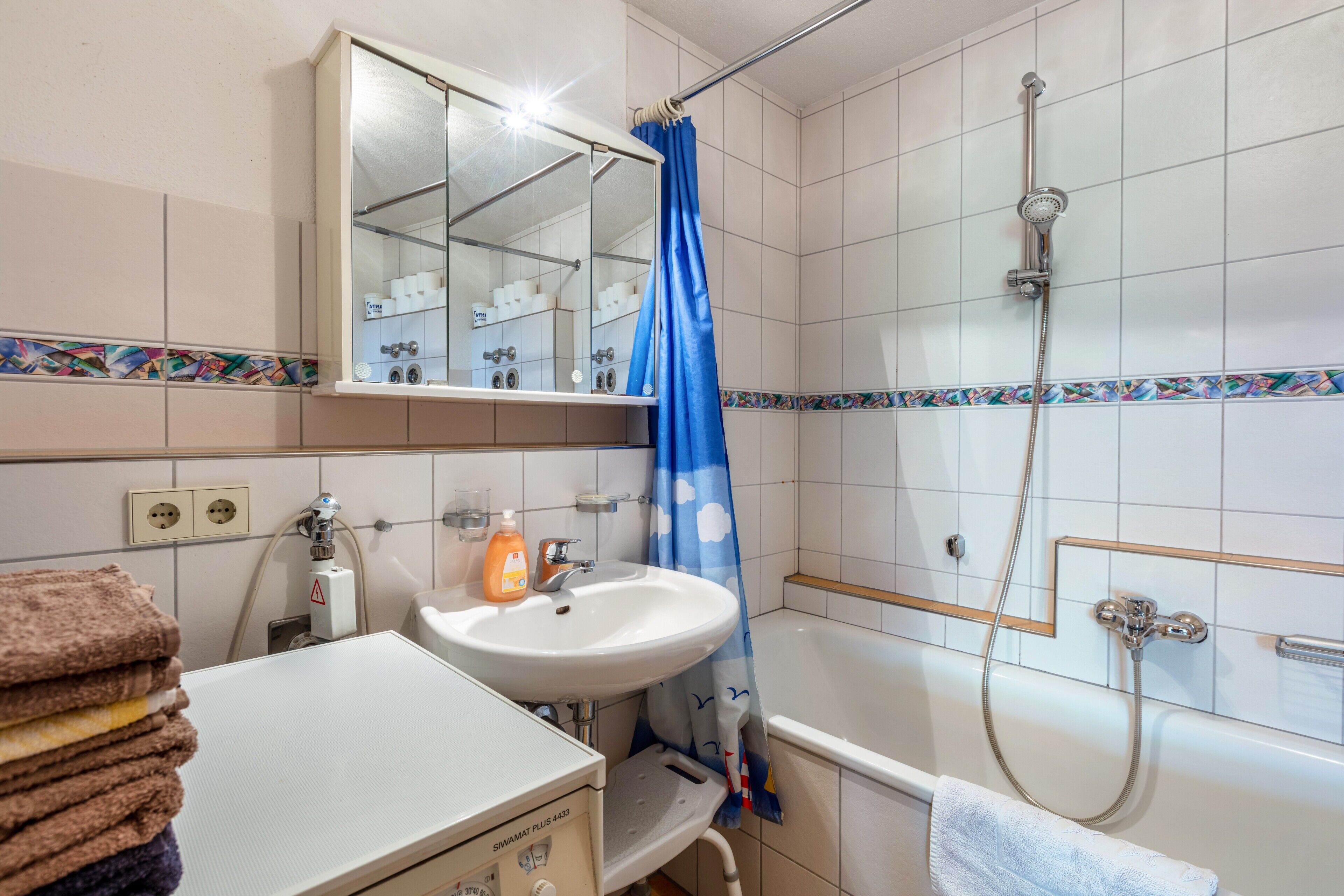 A bathroom with a sink, mirror, shower, and a towel rack.