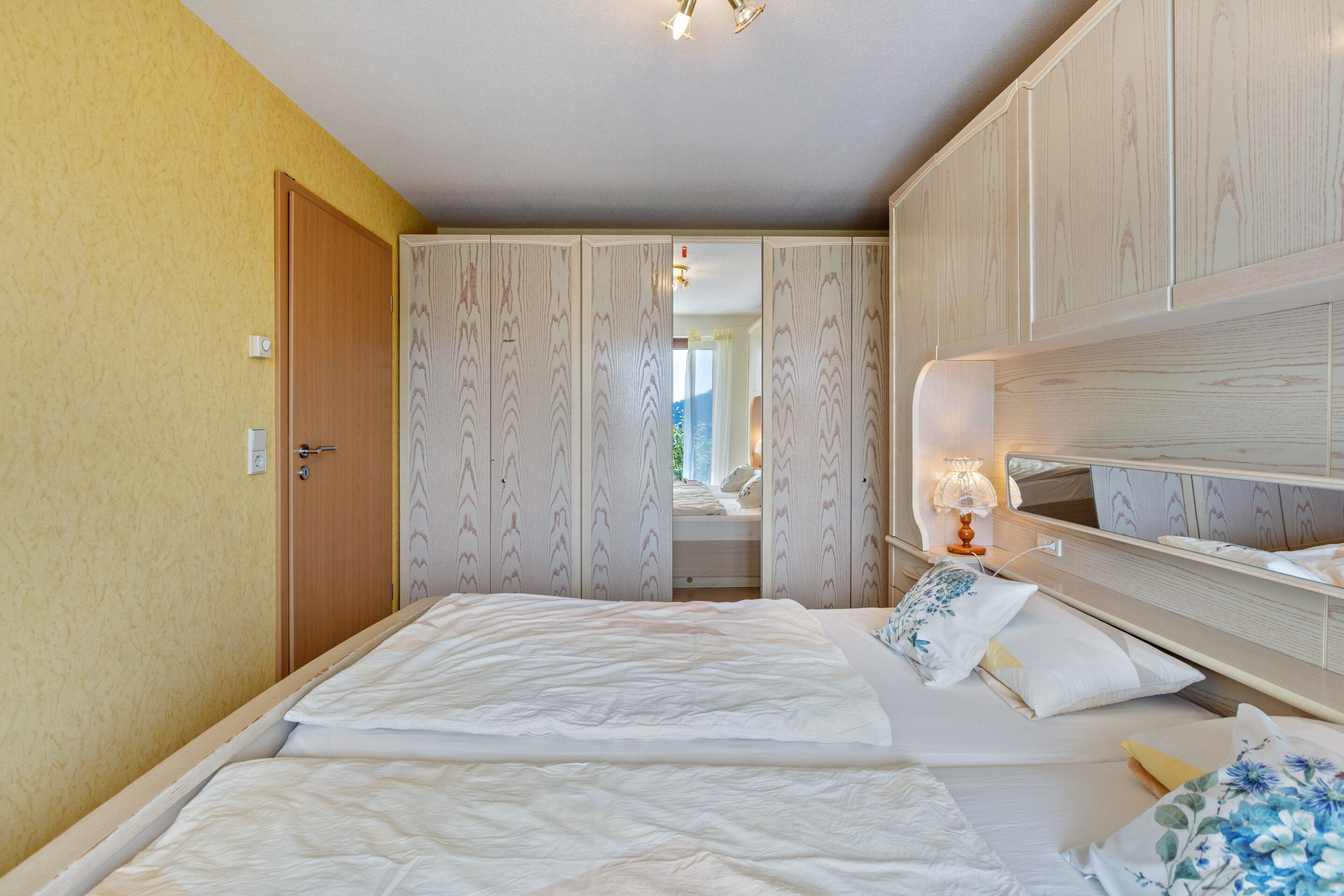 Une chambre à coucher comprenant un lit, une armoire, un miroir et une table de chevet avec une lampe.