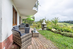 A patio with wicker furniture, a green umbrella, and a view of a garden and hills. - Apartment 'Landblick' with Mountain View, Private Terrace and Wi-Fi (Zell im Wiesental)
