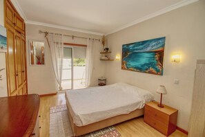 Un dormitorio con cama, mesita de noche, lámpara y una pintura marina.