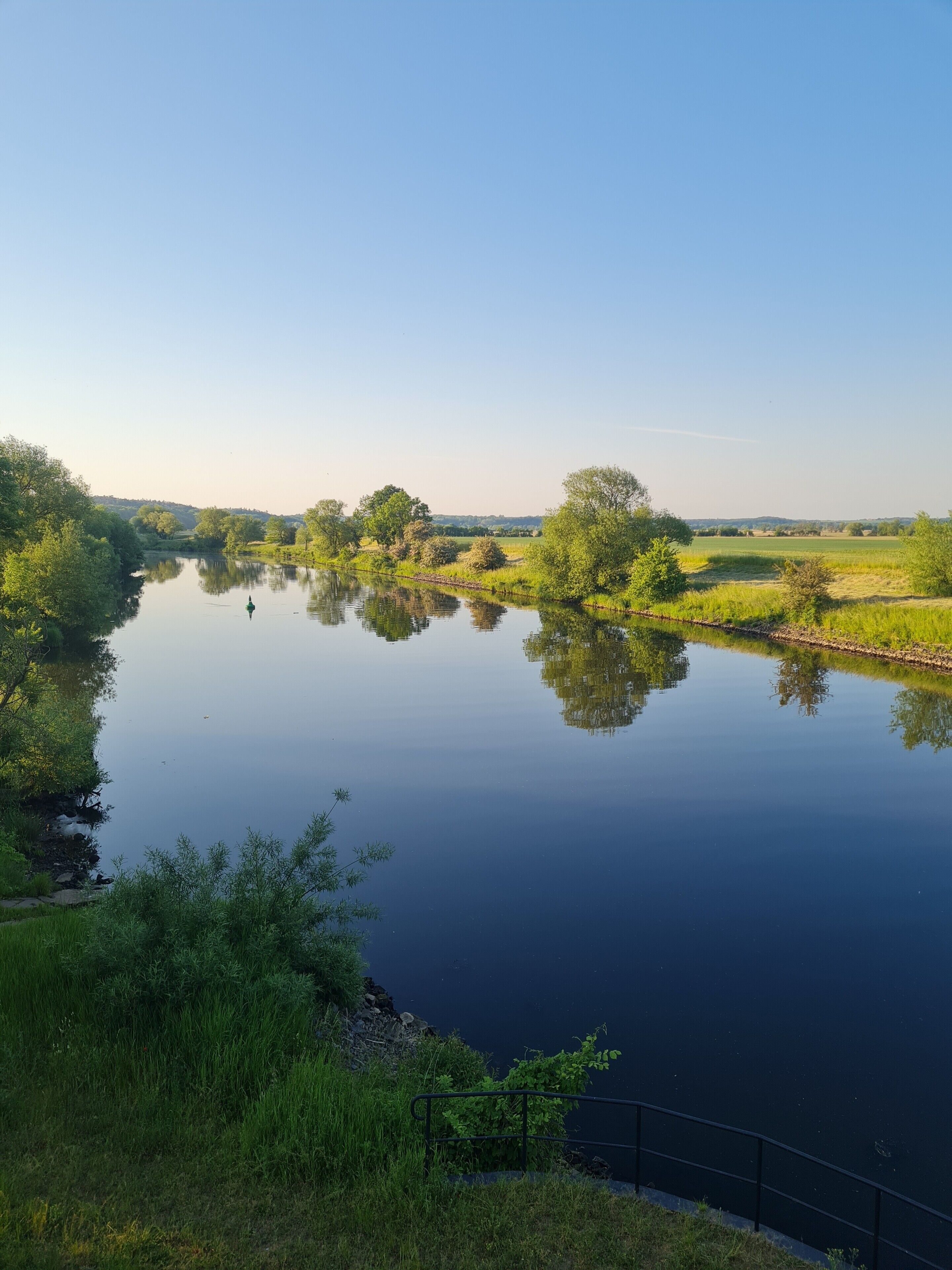 Une rivière paisible, bordée de chaque côté par des arbres et des champs.