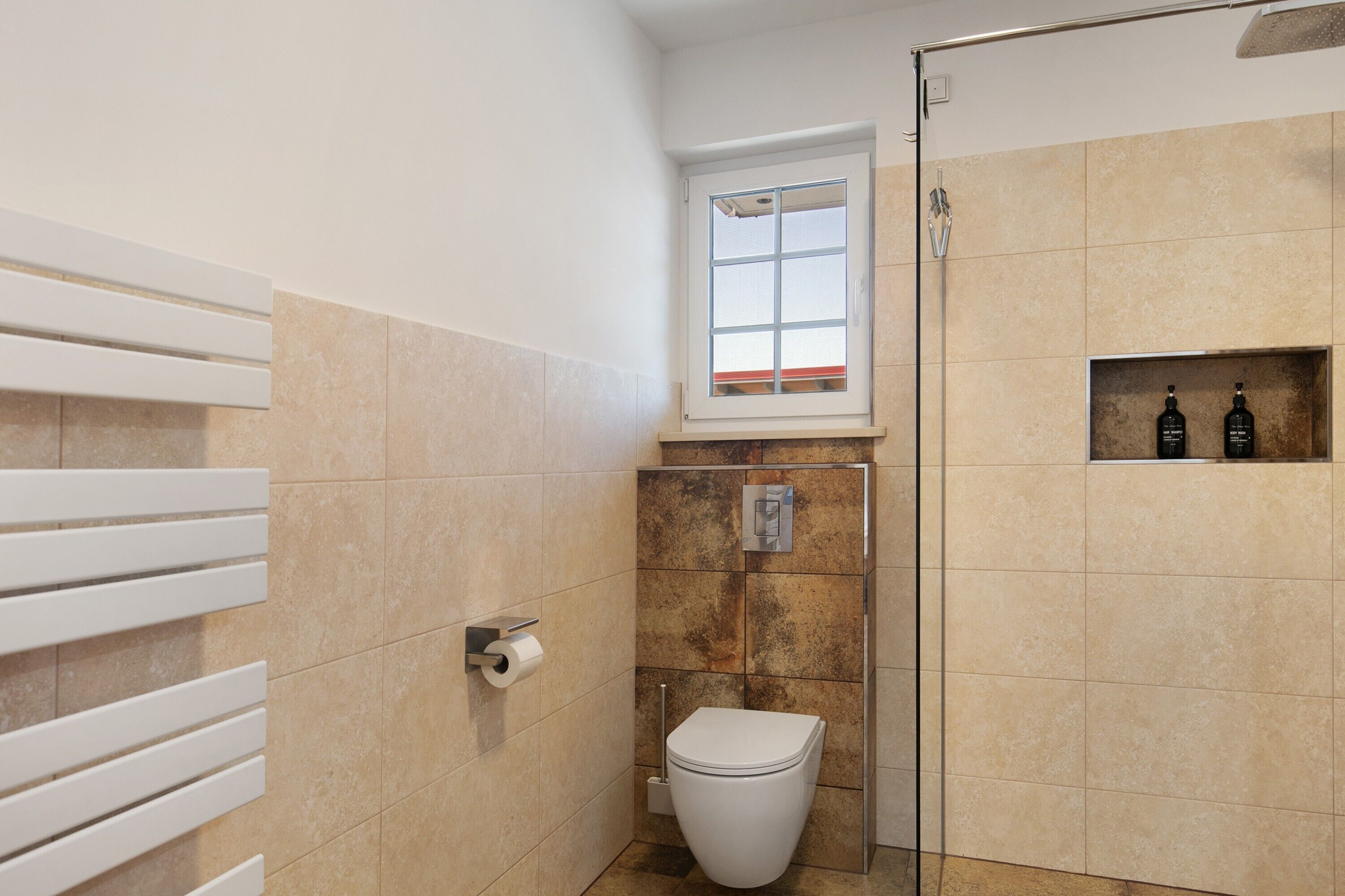 A bathroom with a toilet, a shower, a window, and a shelf with bottles.