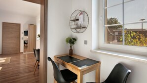 Una habitación con una mesa de madera, dos sillas negras, una planta pequeña y una estantería metálica en la pared.