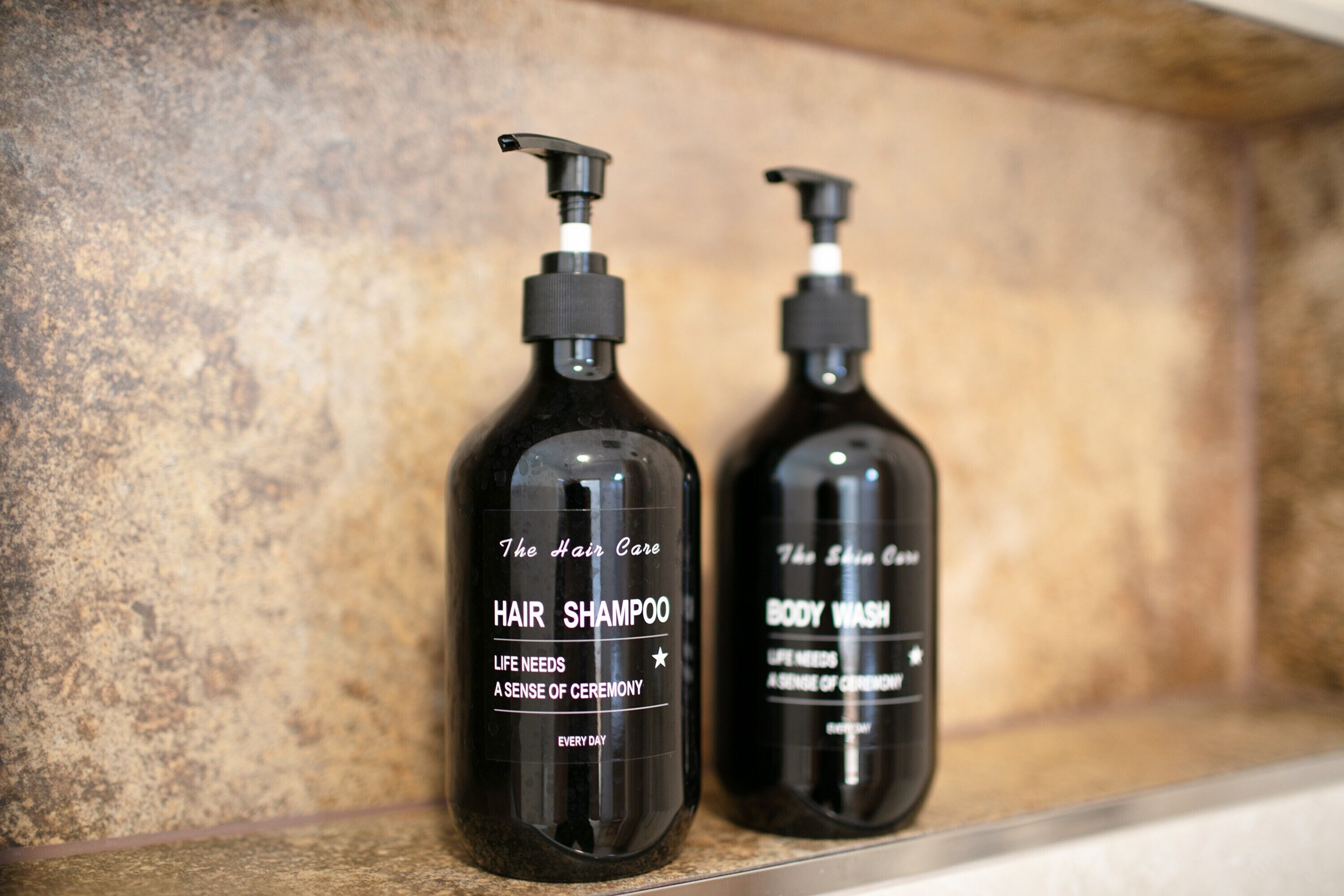 Deux bouteilles noires contenant des produits de soins pour les cheveux et le corps, posées sur une étagère.