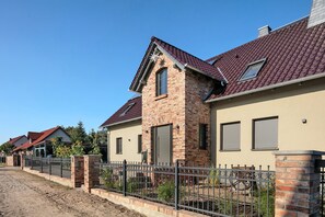 En bostadsgata med hus byggda av tegel, ett staket av metall och en klar, blå himmel.