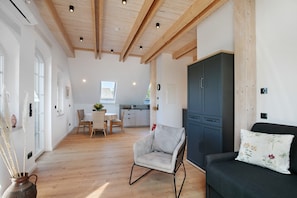 A spacious room with wooden beams, a dining area, and a dark-colored sofa with a floral pillow. - Apartment 'Sonnenblume' with Shared Garden, Balcony and Wi-Fi (Lunow-Stolzenhagen)