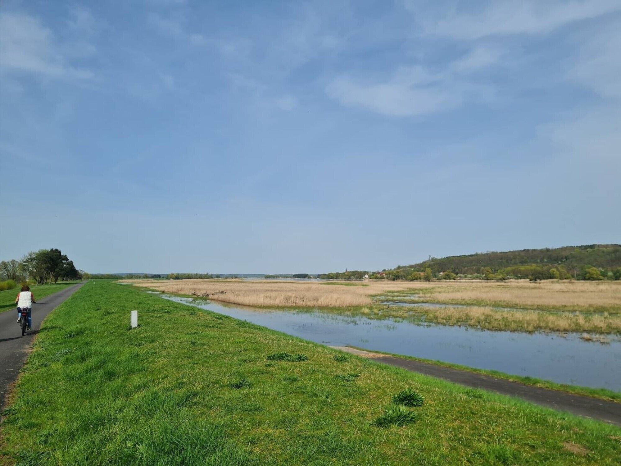 A rural landscape with a paved path, grassy areas, and a water body.