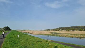 A rural landscape with a paved path, grassy areas, and a water body.