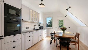 A modern kitchen with white cabinetry, black appliances, and a dining area with a round table and chairs. - Apartment 'Flieder' with Shared Garden, Balcony and Wi-Fi (Lunow-Stolzenhagen)
