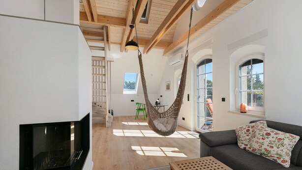 A modern living room with a hanging chair, a sofa with floral cushions, a fireplace, and large windows allowing natural light. - Apartment 'Flieder' with Shared Garden, Balcony and Wi-Fi (Lunow-Stolzenhagen)