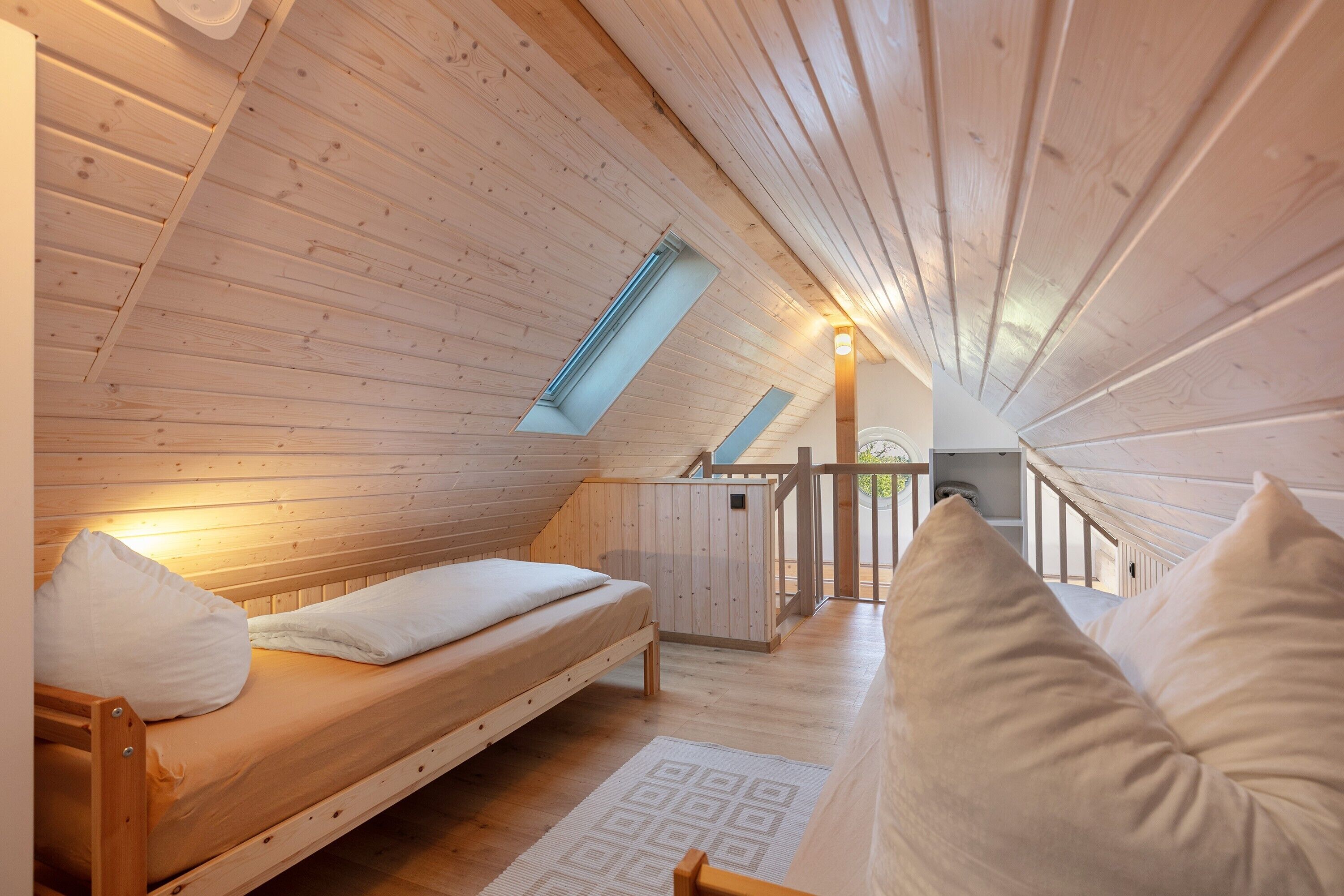A wooden room with a bunk bed, a skylight, and a staircase leading to an upper level.