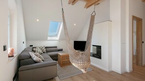 A modern living room with a sofa, a hanging chair, a television, and a fireplace. - Apartment 'Flieder' with Shared Garden, Balcony and Wi-Fi (Lunow-Stolzenhagen)