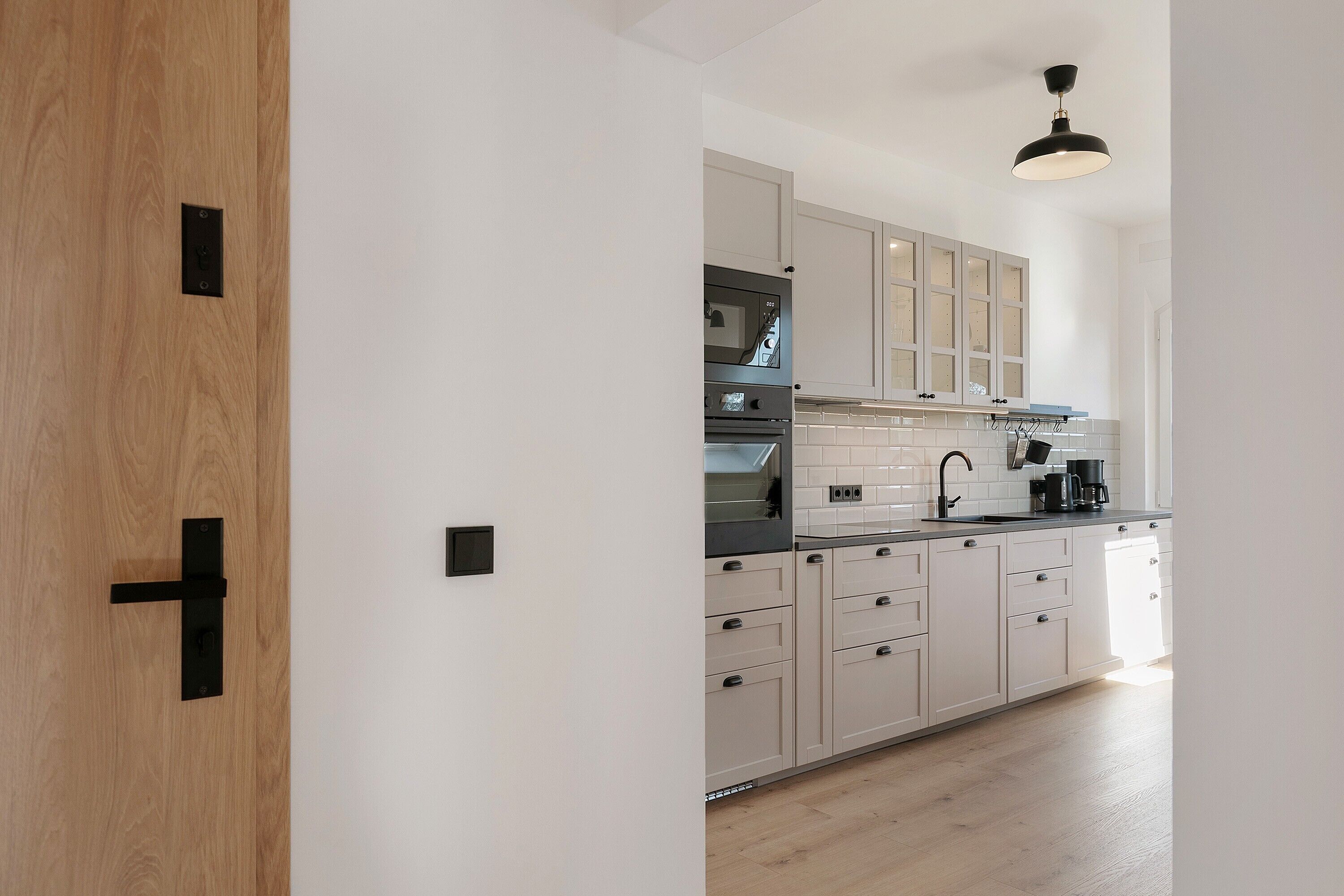Een moderne keuken met witte kasten, een zwart aanrecht en een houten deur.
