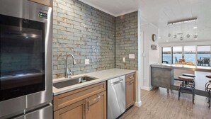 Eine moderne Küche mit Edelstahlgeräten, einer Ziegelrückwand, Holzschränken und Blick aufs Wasser.